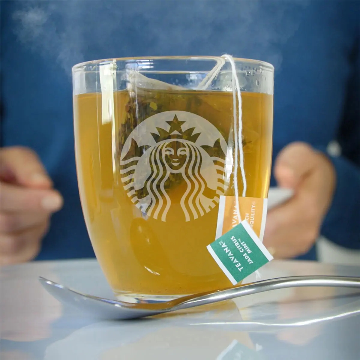 starbucks glass mug with steaming tea and a spoon.