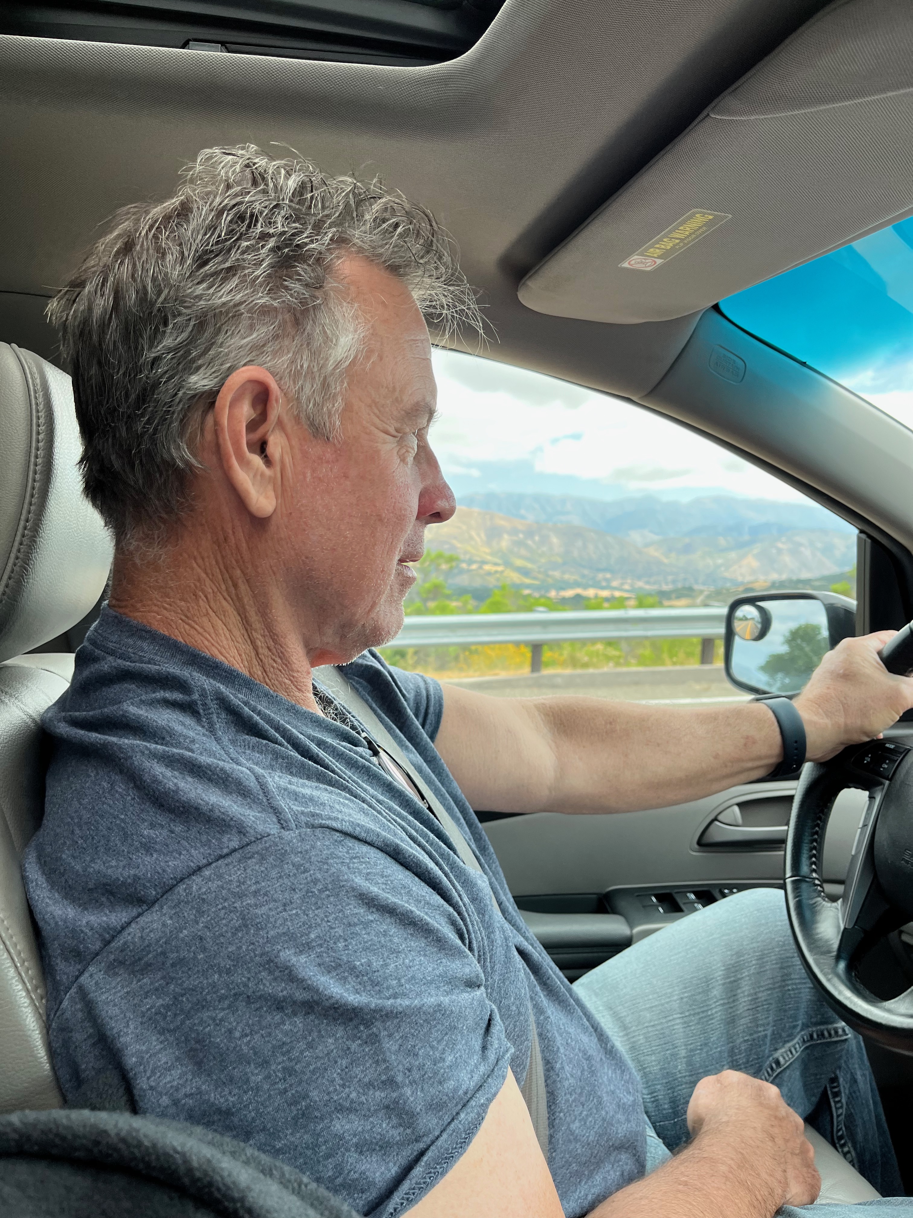 side view of man driving with mountains and clouds in the background.
